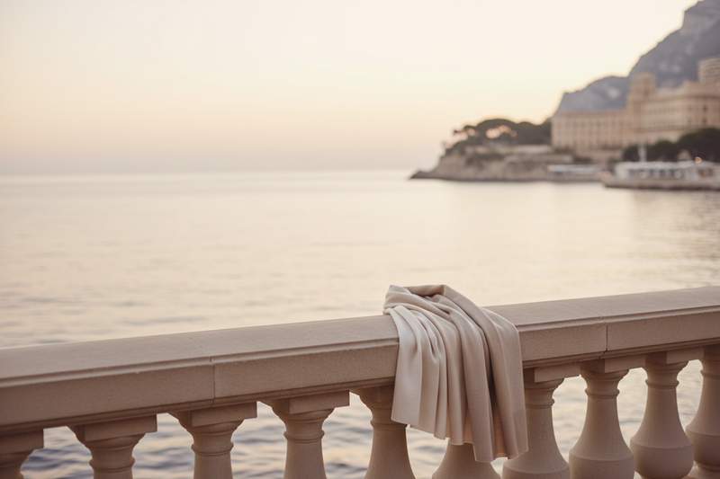 Soft, warm editorial photograph of the Monaco coastline at sunrise, muted champagne tones, gentle blur, quiet-luxury mood, minimal composition, crema palette, Loro Piana campaign aesthetic.